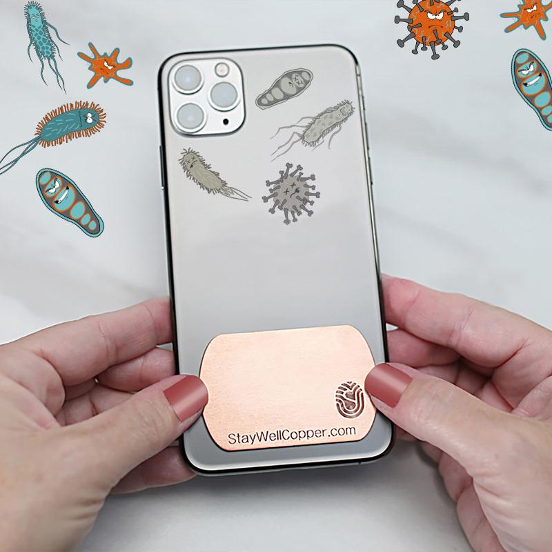 Hands touching phone case with 2" x 1.5" Adhesive Phone Patch made in USA from natural antimicrobial copper attaches to germy devices we touch most. Shows live germs around case and dead germs on case. Sanitizers, Chemical Free, Lasts Forever. Recyclable. Kills 99.9% of Harmful Bacteria. EPA registered. 